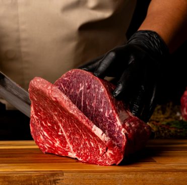 The,Butcher,Wearing,Black,Gloves,Cuts,The,Meat,With,Knife